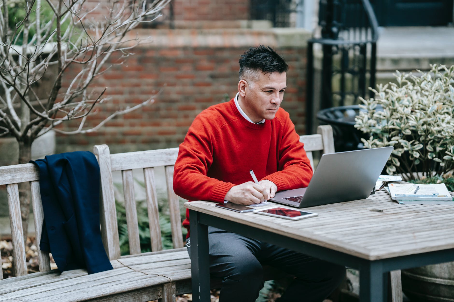 photo of man writing while looking on laptop